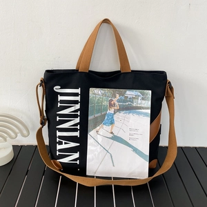 Détail d'un sac cabas en toile noire avec lanières brunes et lettrage blanc très stylé