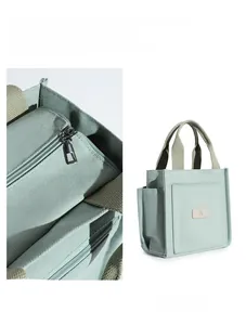 Detail view of a light green canvas tote bag featuring a zip closure and front pocket