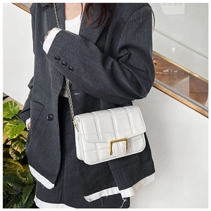Detail of white quilted handbag with gold square buckle and chain strap on a model