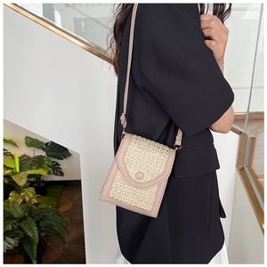 Detail of woven straw and pink leather crossbody phone bag shown on a model