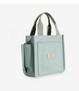 Detail view of mint green canvas tote with a large front pocket and leather N patch