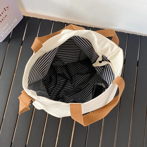 Vue détaillée du cabas en toile montrant la doublure rayée et la poche zippée interne