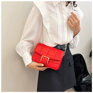 Detail shot of a red quilted crossbody bag with a gold metal clasp and thin chain strap