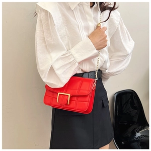 Detail of red quilted crossbody bag featuring a golden square buckle and chain strap