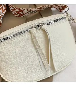 Close-up of beige lychee grain leather chest bag with silver zippers and wide patterned strap