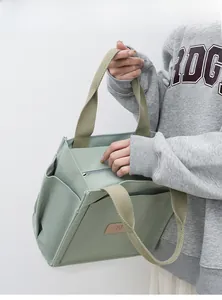 Detail view of mint green canvas tote bag featuring brown leather N logo and side pocket