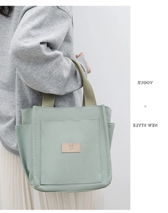 Detail view of green canvas tote bag with brown leather N logo and woven handles