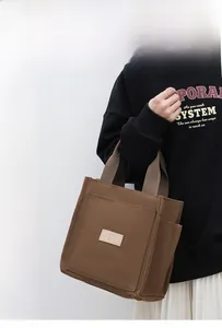 Detailed side view of brown canvas tote bag featuring a leather patch and side pocket