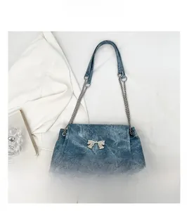 Detail of silver butterfly bow charm and metallic chain strap on navy blue denim tote bag