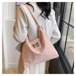 Pink matte tote bag with gold bow clasp worn by model in a natural indoor setting