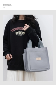 Close-up of gray canvas tote bag featuring a leather N logo patch and side pocket