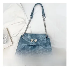 Close-up of blue denim shoulder bag with silver butterfly buckle and phone for scale
