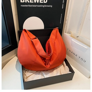 Detailed close-up of an orange crescent hobo bag with a tassel zipper in a gift box