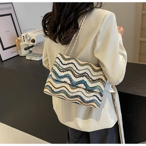 Detail of multi-color woven tote bag with wavy patterns and metal chain strap shown on model