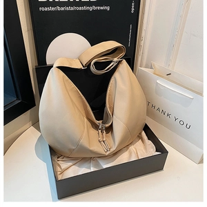 Close-up of beige minimalist dumpling bag with dual tassels in a gift box packaging