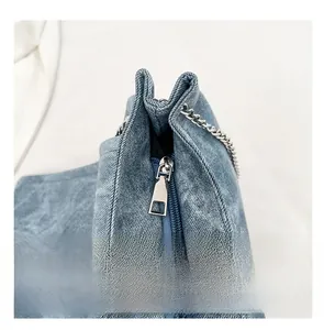 Detail of blue denim tote bag featuring a smooth silver metal zipper and chain strap