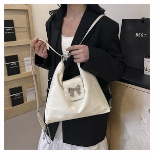 Close-up of a white patent leather shoulder bag featuring a silver metal bow accent
