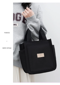 Detail of black canvas tote bag featuring leather patch with letter N branding and side pockets