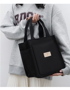 Detail view of black canvas tote bag featuring side pocket and leather letter N patch