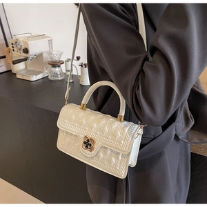 Detailansicht der cremeweißen Stepptasche mit goldenem Kleeblatt-Verschluss und Griff