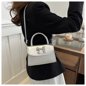Silver metallic crossbody bag with bow buckle decoration worn by model in minimalist room