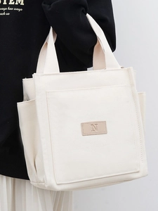 Minimalist off-white canvas tote bag with brown leather N patch for daily commuting