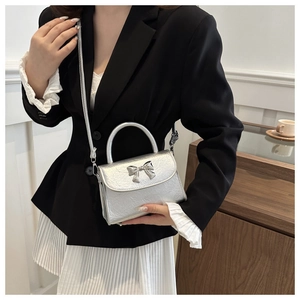Silver bow handbag with pleated texture shown on model in a stylish indoor setting