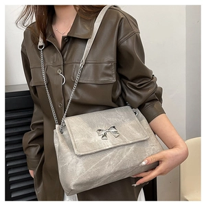 Detail of grey crossbody bag featuring a silver metal butterfly bow and chain strap