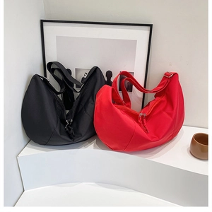 Detail view of stylish half-moon crossbody bags in red and black on a minimalist stand