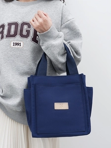 Dark blue canvas tote bag with leather 'N' patch held by model against white wall