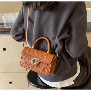 Detail der braun gesteppten Handtasche mit Kleeblatt-Goldschnalle und Webstruktur