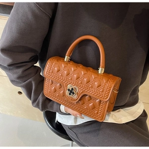 Detailansicht einer karamellfarbenen Stepptasche mit goldenem Kleeblatt-Verschluss