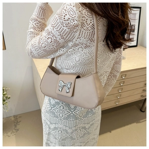 Détail d'un sac sous le bras beige avec un fermoir nœud argenté et cuir lisse poli