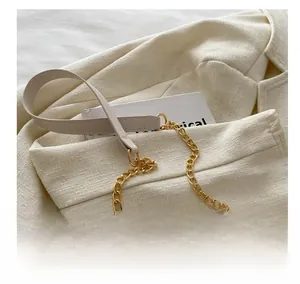 Detail of a chic cream leather strap with gold chain links on a beige blazer texture