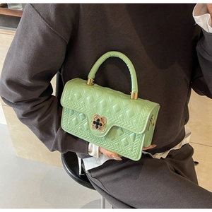 Detail einer minzgrünen Stepphandtasche mit goldenem Blumenschloss, gehalten von Model
