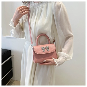 Close-up of a pink mini crossbody bag with a silver bow on white dress background