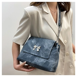 Detail of blue denim shoulder bag with silver butterfly charm and chain strap on a model