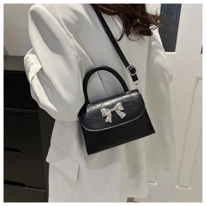 Detail of black crossbody bag with silver bow accent on a white blazer outfit