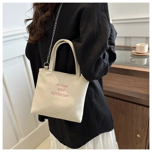 Détail du sac à main brodé crème avec bandoulière chaîne et texte strive and optimism