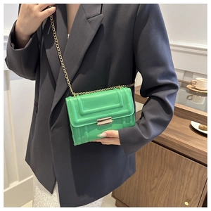 Detailed view of bright green textured square bag with gold chain strap on grey blazer