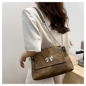Detailed close-up of brown textured leather shoulder bag featuring silver butterfly buckle