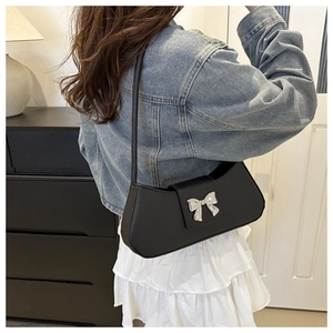 Détail du sac sous l'aisselle noir avec boucle noeud argenté sur une veste en jean