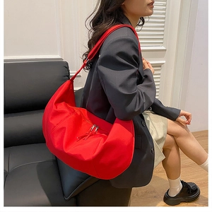 Close-up of a large red nylon dumpling bag worn by a model in a modern indoor setting