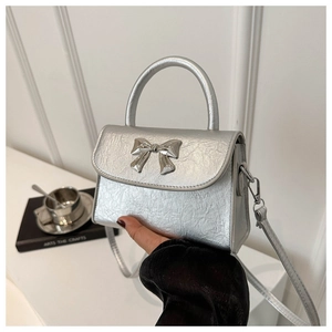 Detail shot of the silver metallic bow on a glossy leather crossbody handbag