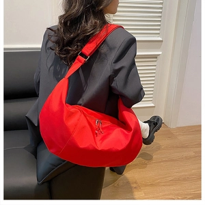 Detail of red crescent shoulder bag featuring dual zippers and adjustable wide strap