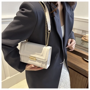 Detail of a beige square crossbody bag with gold lock and metal chain strap on model