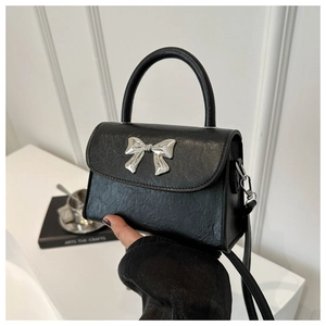 Close-up of black leather texture and silver metal bow ornament on a stylish handbag