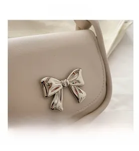 Close-up of beige leather bag featuring a polished silver metal bow pendant detail