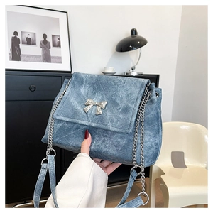Detail of blue denim shoulder bag featuring silver butterfly buckle and metal chain strap