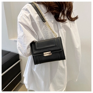 Detail of black leather square bag with vertical texture and gold chain strap on model